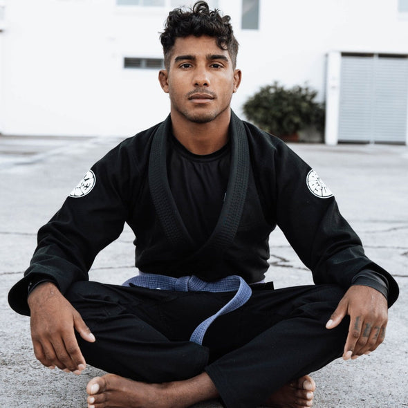 Black martial arts gi with blue belt, worn by a person sitting outdoors, with obscured facial identity.